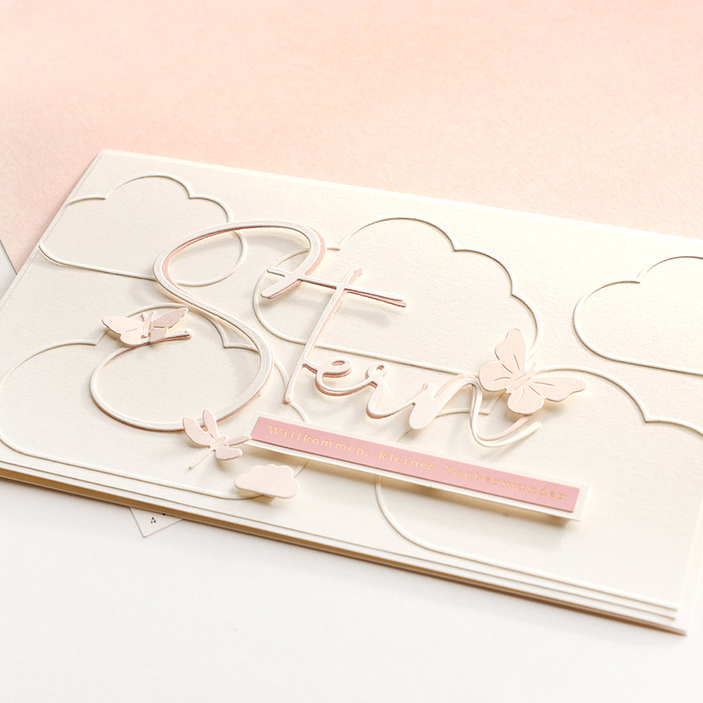 Elegante Karte von Alexandra Renke aus Designpapier mit dem Schriftzug "Stern", Schmetterlingen, Wolken und einem rosa Etikett mit "Willkommen, kleines Zauberwunder".