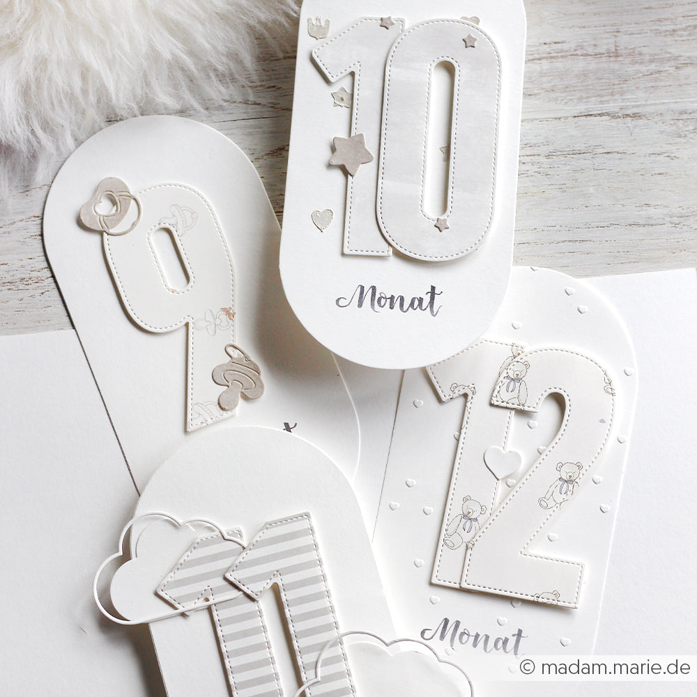 Weiße Meilensteinkarten von Alexandra Renke mit den Motivstanze Zahlen 9, 10, 11 und 12, verziert mit Sternen, Wolken und Bären für einen charmanten Touch.