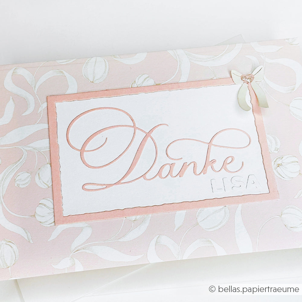 Auf einer rosa-weißen Blumenkarte von Alexandra Renke steht in eleganter Schrift "Motivstanze Kalligrafisch Danke Lisa", mit einer kleinen Schleife als Akzent und hochwertigem Designpapier für ein edles Finish.