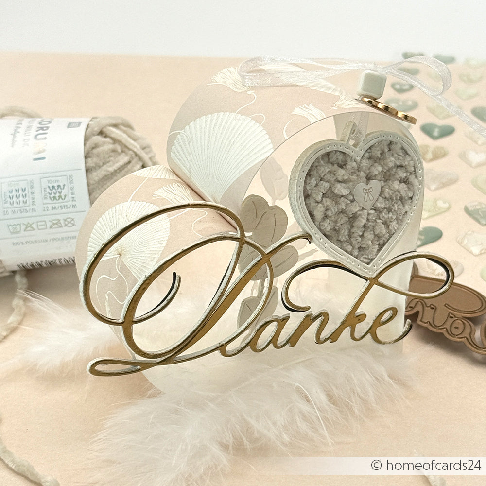 Dekorative Karte von Alexandra Renke mit "Kalligrafisch Danke" in Gold, Herzverzierung, Federn und Garnspule - ideal, um Ihre liebsten Designpapiere und kreativen Stanzsysteme hervorzuheben.