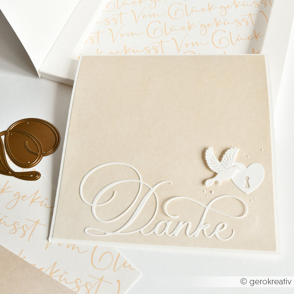 Die quadratische beigefarbene Dankeskarte von Alexandra Renke zeigt ein weißes "Danke", eine Taube und ein Herz mit Schlüsselloch. Sie wurde mit DieCut Systemen hergestellt und mit der Motivstanze Kalligrafisch Danke veredelt.
