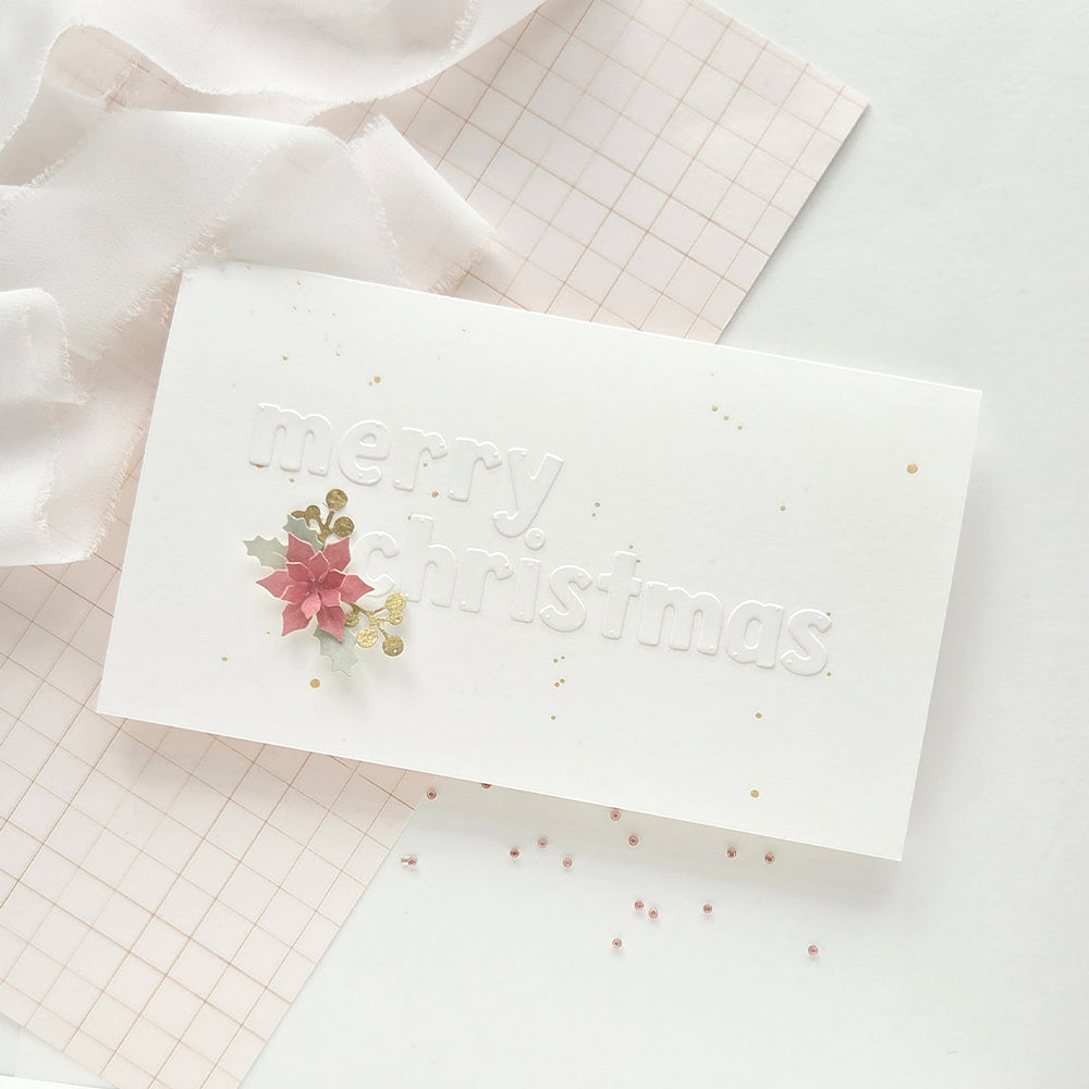 Eine weiße, geprägte Weihnachtskarte mit Designpapieren und einer kleinen Papier-Weihnachtssternblüte.
