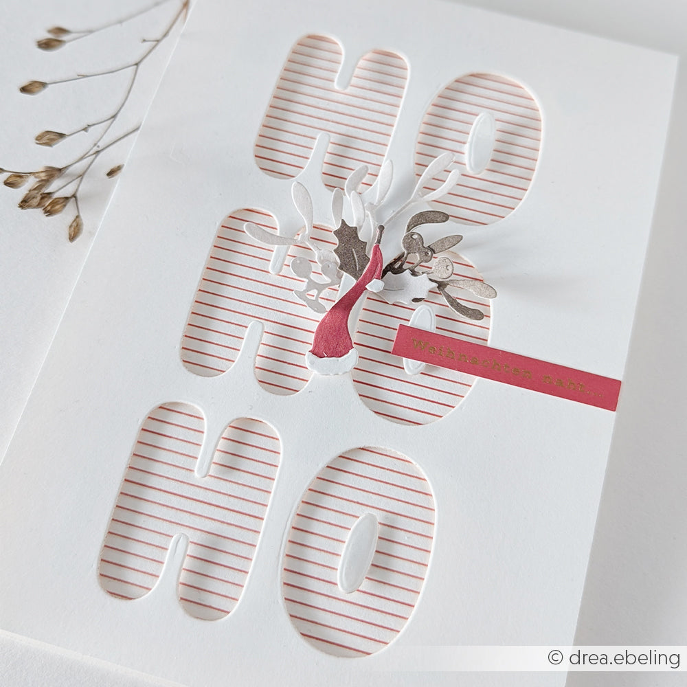 Weihnachtskarte mit ausgestanztem HO HO HO-Schriftzug auf rot gestreiftem Designpapier und Mistelzweig.