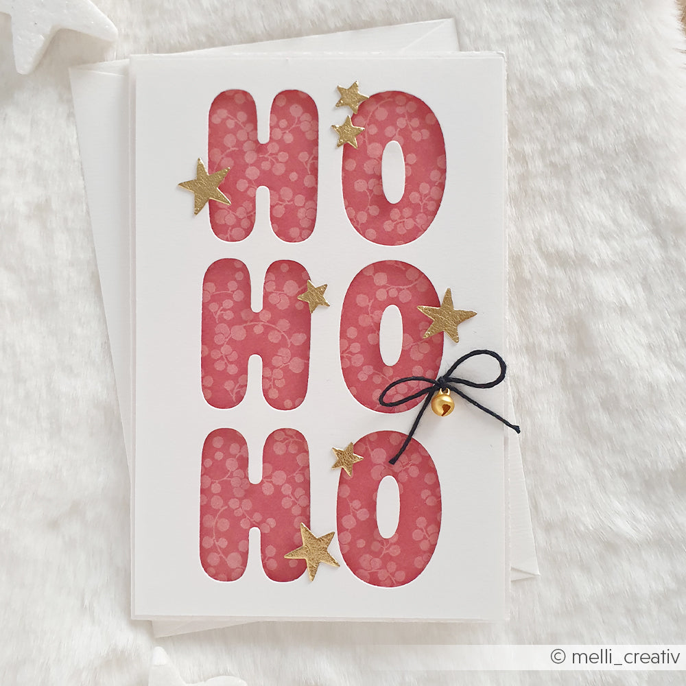 Eine handgefertigte Grußkarte aus Designpapier mit roter HO HO HO-Schrift und goldenen Sternen.