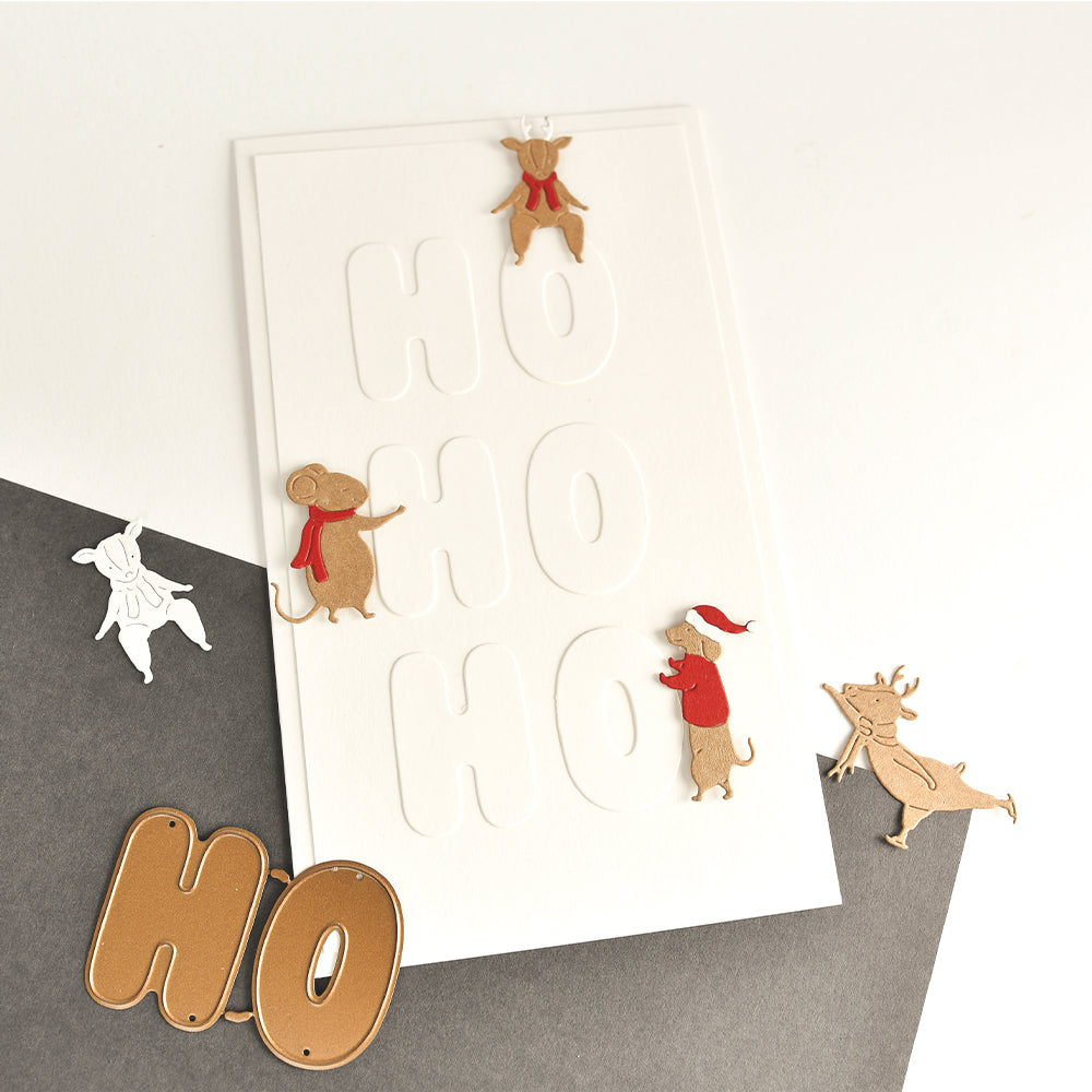 Eine Karte mit geprägtem „HO HO HO“-Schriftzug, verziert mit aus Papier ausgestanzten Rentieren und Mäusen, die mit Motivstanze gestaltet wurden.