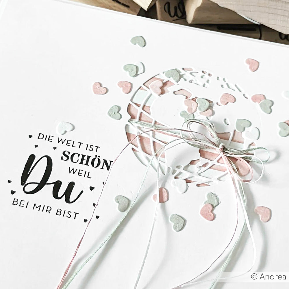 Weiße Karte von Alexandra Renke mit pastellfarbenem Herzkonfetti, einer ausgeschnittenen Weltkugel und dem Text "Die Welt ist schön, weil du bei mir bist" - ideal für Papierprojekte oder in Kombination mit Ihrem Lieblingsholzstempel.
