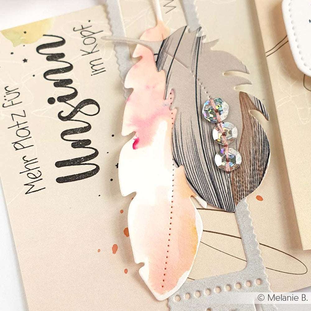 Nahaufnahme einer dekorativen Karte mit einem Federausschnitt, Pailletten und deutschem Text auf beigefarbenem Hintergrund - eine ideale Inspiration für Papierprojekte oder Ihren Lieblingsholzstempel. Entwurf von Alexandra Renke.