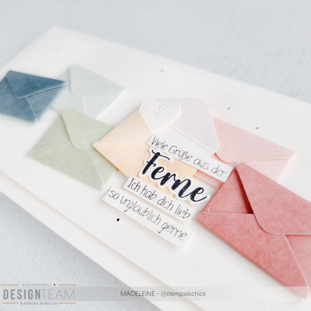 Bunte Papierumschläge von Alexandra Renke und eine Karte mit deutschem Text, ideal für Papierprojekte, werden auf einer weißen Fläche präsentiert.