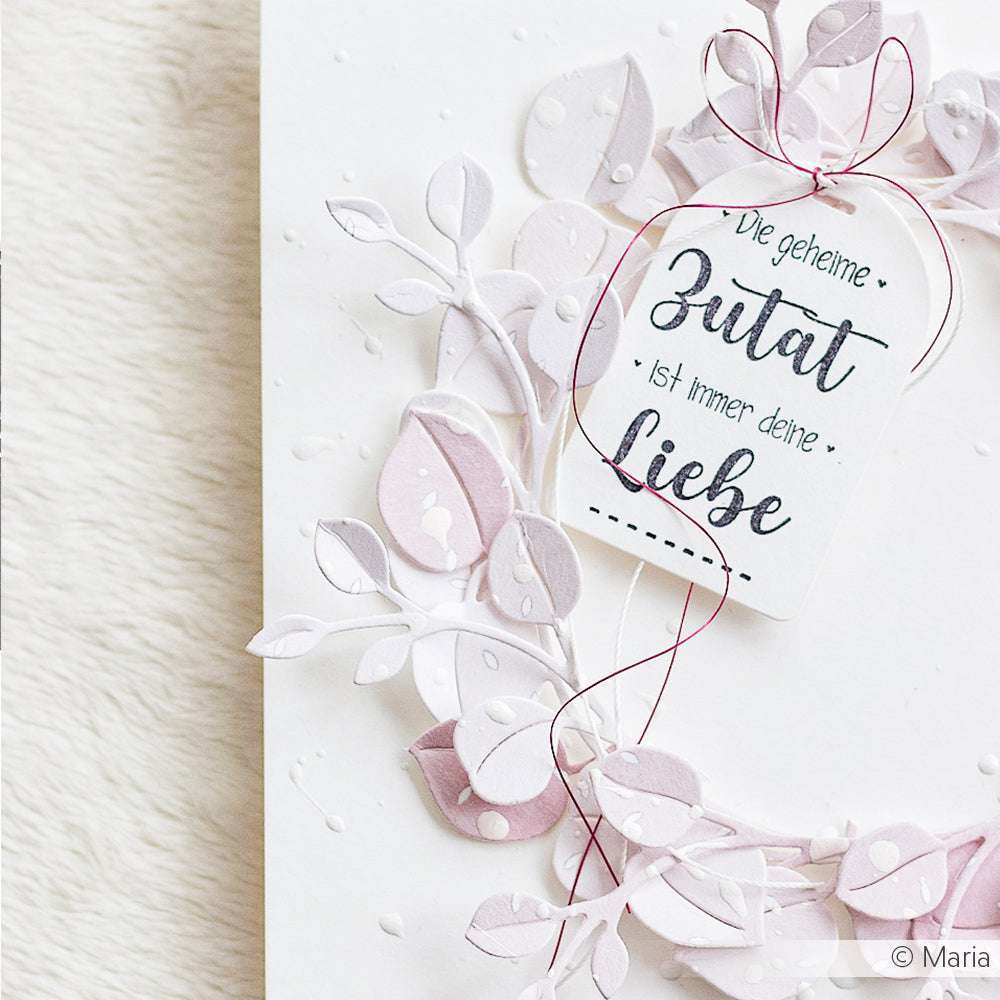 Handgemachte Karte von Alexandra Renke mit pastellfarbenen Papierblättern, roter Schnur und deutschem Liebestext auf weißem, strukturiertem Hintergrund. Die detailreichen Designs mit Holzstempeln und Stempelkissen sorgen für ein künstlerisches Flair.