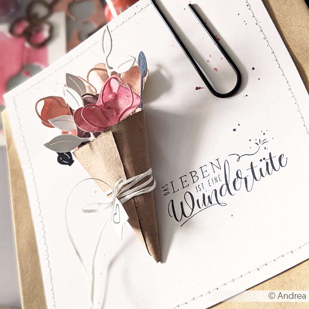 Die handgefertigte Karte von Alexandra Renke zeigt einen Papierstrauß und den deutschen Satz "Das Leben ist eine Wundertüte" auf weißem Hintergrund.