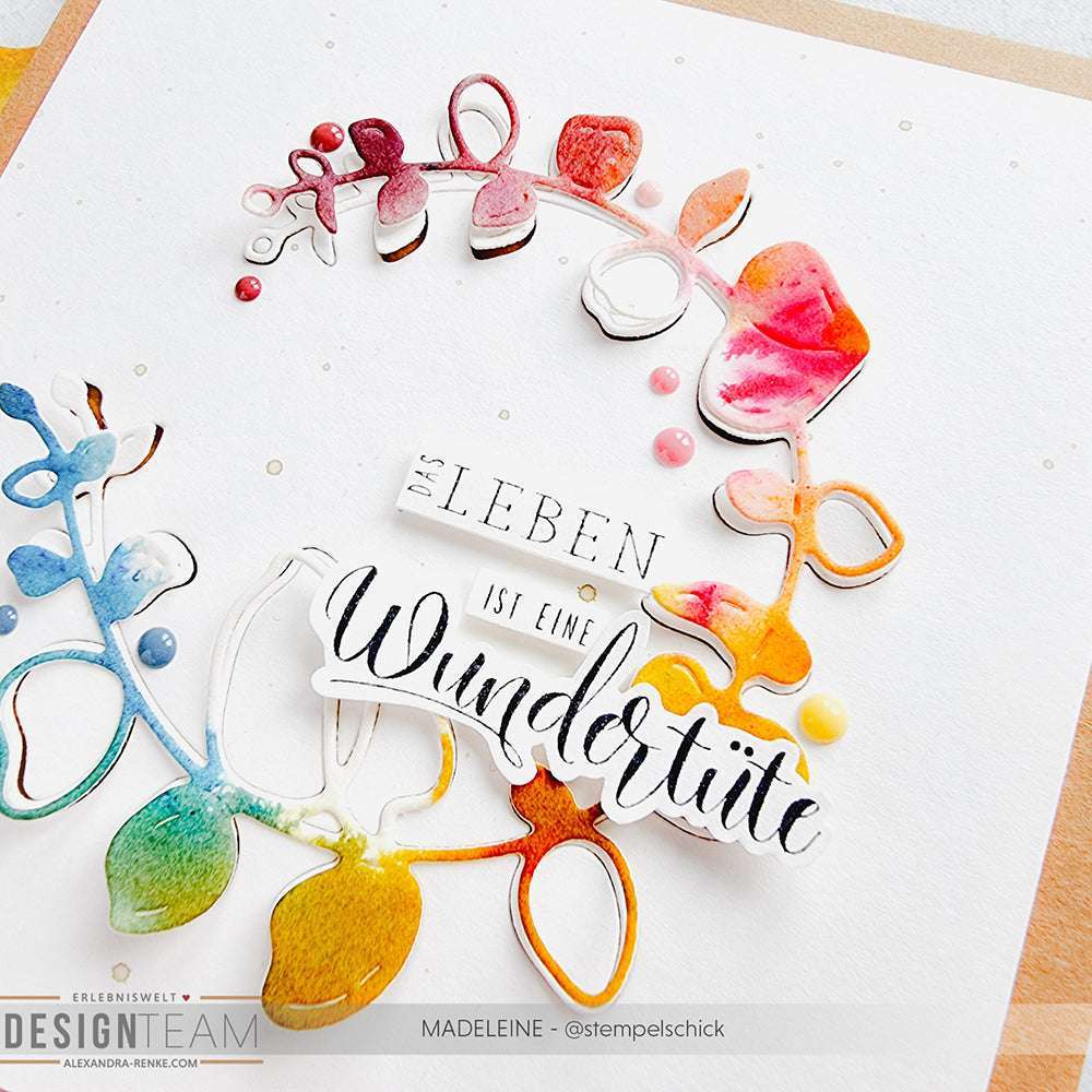Ein aquarellierter Blumenkranz umgibt den Satz "Das Leben ist eine Wundertüte" auf weißem Hintergrund - ein charmantes Design von Alexandra Renke, das sich ideal mit Ihrem Lieblingsholzstempel oder Stempelgummi kombinieren lässt.