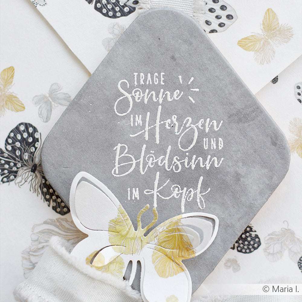 Eine graue Karte mit deutschem Text und einem Schmetterlingsausschnitt, der mit Schmetterlingsmotiven verziert ist, passt hervorragend zu einem hochwertigen Alexandra Renke Stempel Sonne im Herzen" aus Holz und sorgt für einen eleganten Touch.