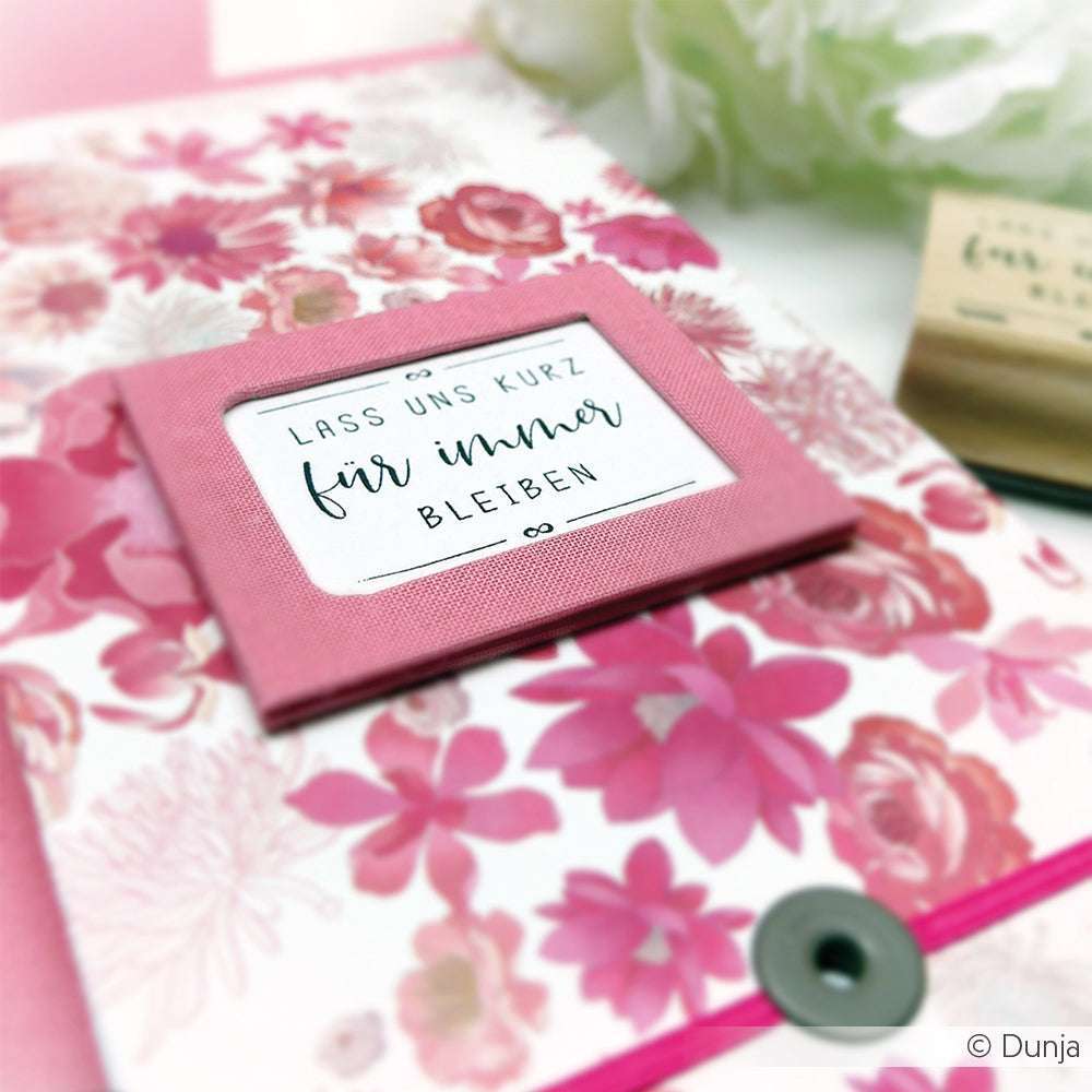 Rosafarbene Blumenkarte von Alexandra Renke mit einem Fenster, das den deutschen Text "Lass uns kurz für immer bleiben" zeigt. Geprägt mit hochwertigem Holz und Gummi für ein elegantes Finish.