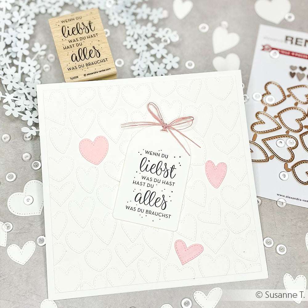 Eine handgefertigte Karte von Alexandra Renke mit geprägten weißen Herzen, rosafarbenen Akzenten, einem mit rosafarbener Schnur gebundenen Spruchanhänger und hochwertigen Holzstempel-Stempelmotiven für eine elegante Note.