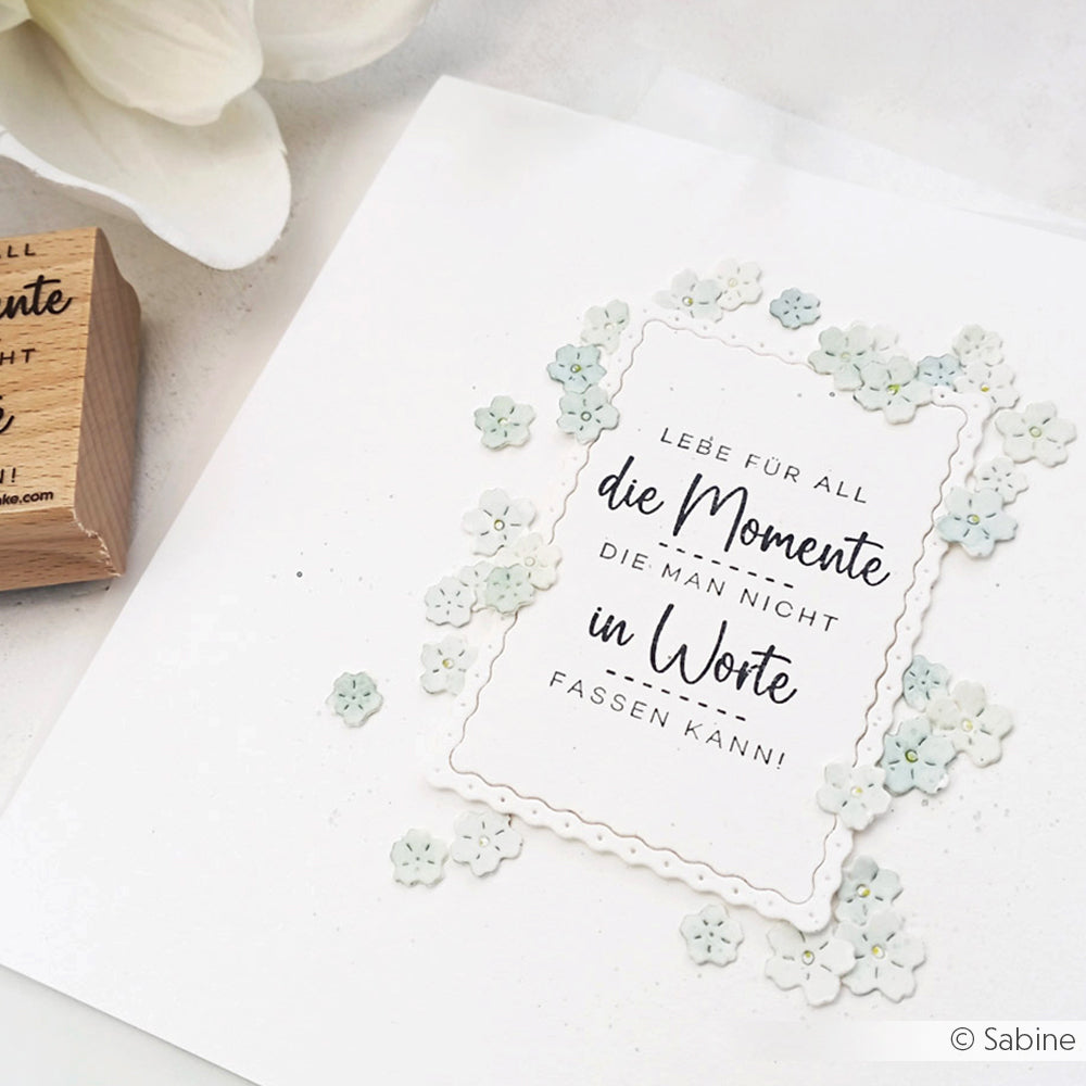 Eine weiße Karte von Alexandra Renke mit einem deutschen Zitat, ideal für Papierprojekte, mit kleinen weißen Blumen am Rand.