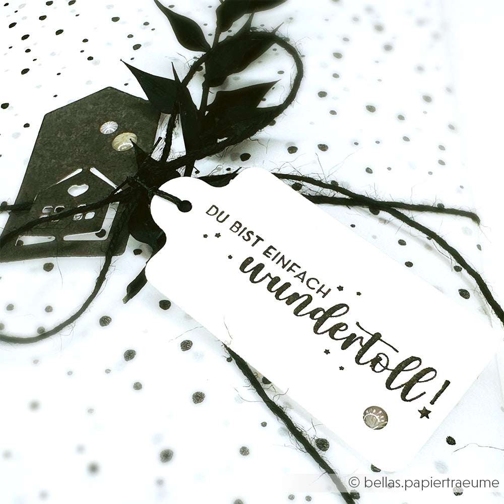 Weißes Geschenk mit schwarzem Band und Anhängern mit Alexandra Renke-Akzenten; auf einem Anhänger steht "Du bist einfach wundertoll!" auf Deutsch.