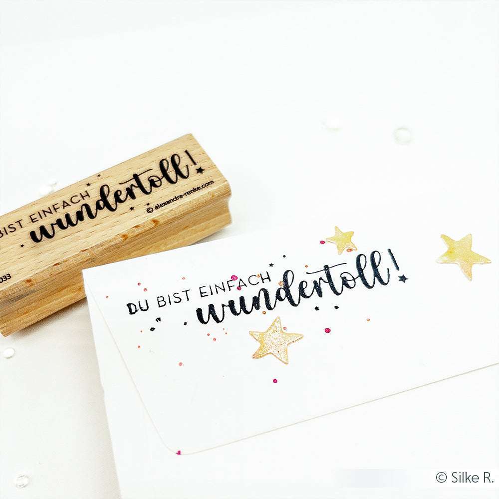 Ein Holzstempel mit Stempelgummi und eine Karte von Alexandra Renke mit dem deutschen Text "Du bist einfach wundertoll!" sowie goldenen Sternen - ideal für liebevolle Papierprojekte.