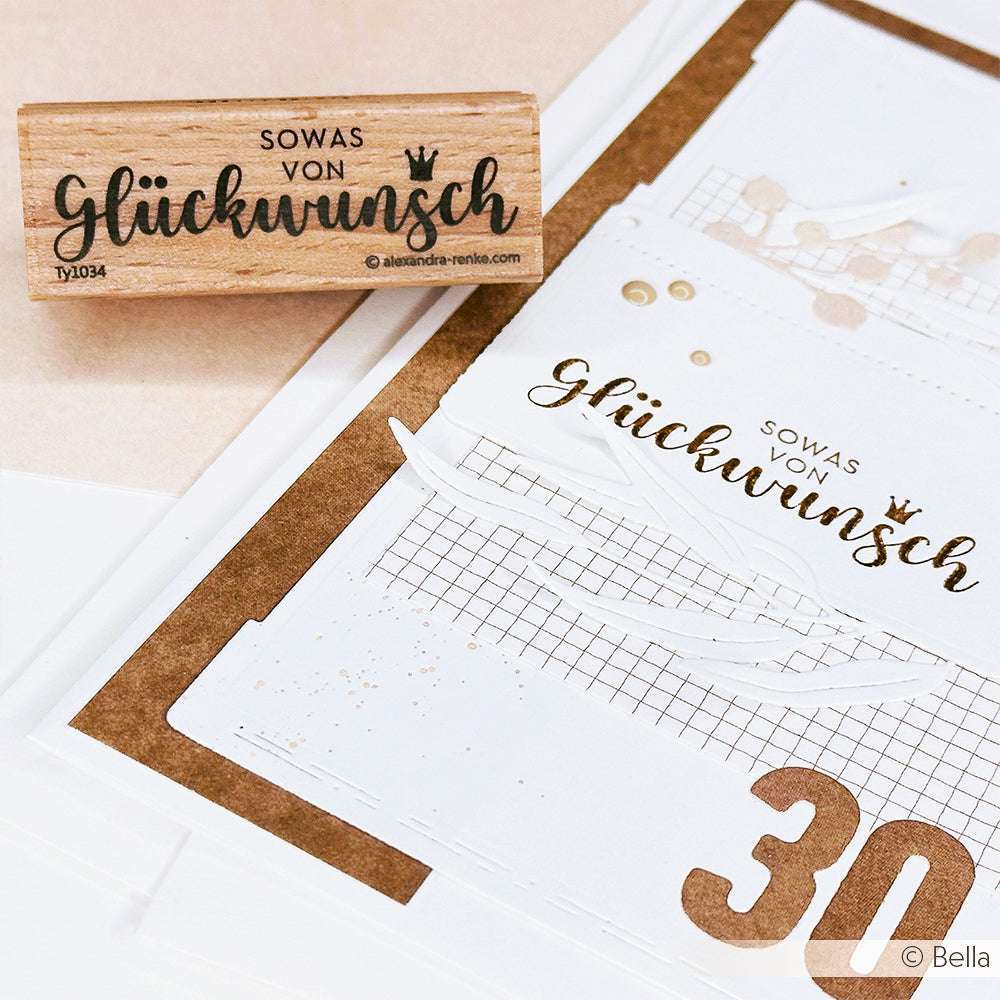 Auf einem Alexandra Renke Holzstempel und einer Karte steht das Wort "Glückwunsch" in eleganter Schrift - ideal, um einen einzigartigen Akzent bei Papierprojekten zu setzen.