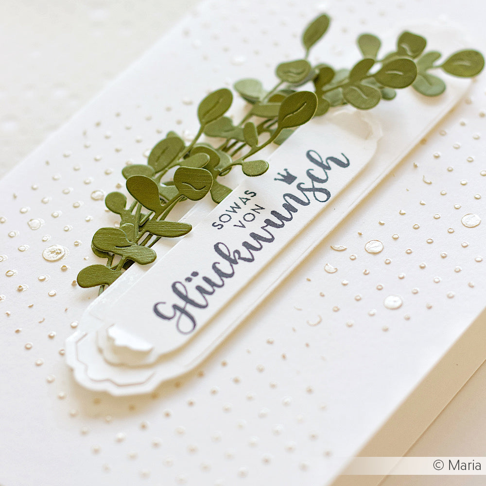 Die weiße Karte von Alexandra Renke zeigt geprägte Punkte, grüne Blätter und "Glückwunsch" in Deutsch auf einem geschichteten Etikett - ideal für Papierprojekte und einfach mit Ihrem Lieblingsholzstempel zu machen.