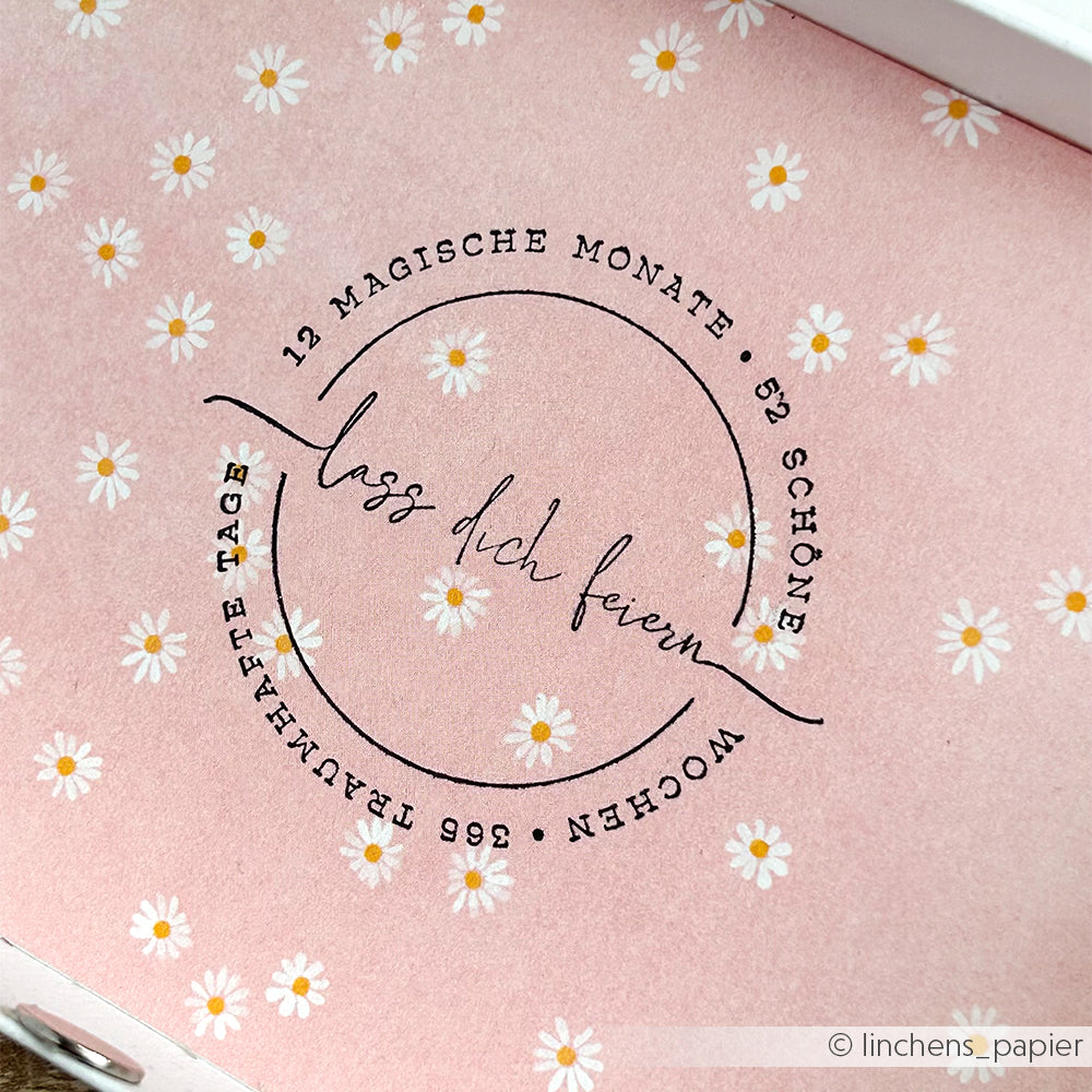 Der rosafarbene Hintergrund von Alexandra Renke zeigt kleine weiße Gänseblümchen und einen deutschen Text in einem zentralen, kreisförmigen Design - ideal für Papierprojekte oder in Kombination mit Ihren Lieblings-Stempelgummis und Holzstempeln.