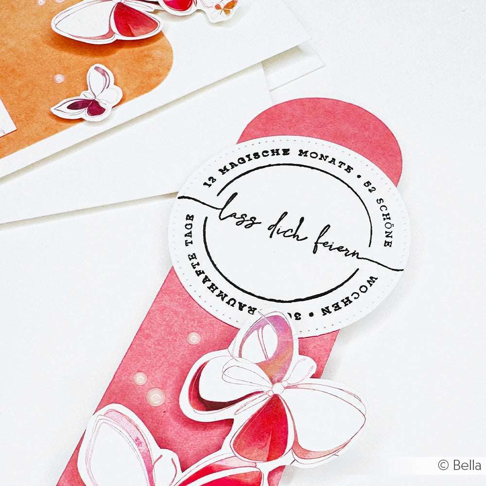 Rosa Schmetterlinge, Papierbasteleien und ein rundes deutsches Textetikett mit hochwertigen Holzstempel-Akzenten von Alexandra Renke zieren dieses rosa Lesezeichen auf weißem Hintergrund.