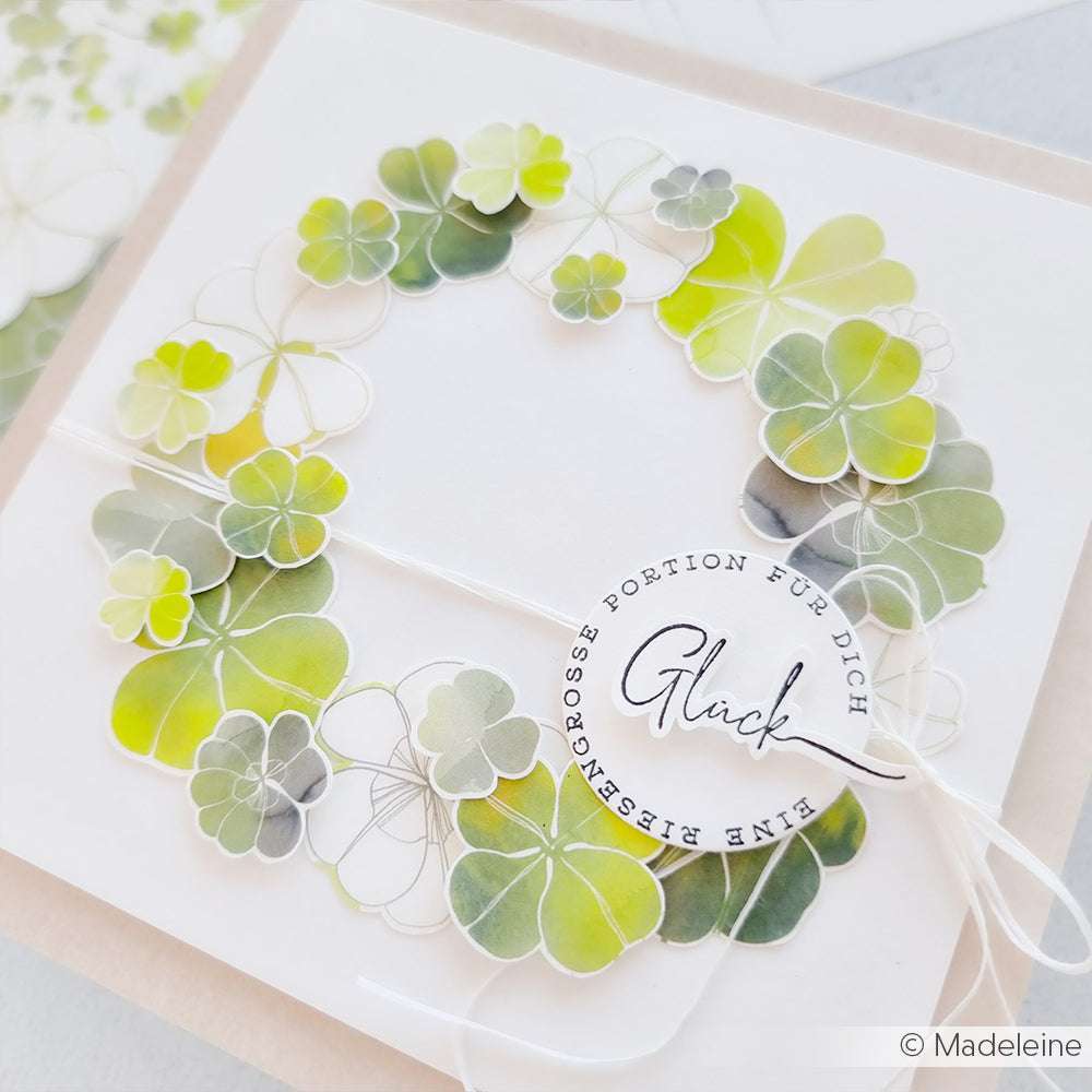 Ein Kranz aus grünen und gelben Aquarellkleeblättern ziert diese weiße Karte von Alexandra Renke mit deutschem Text und dem Wort Glück - ideal für Papierprojekte oder zur Kombination mit Ihrem Lieblingsholzstempel.