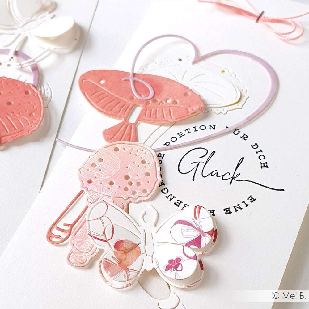 Handgemachte Karte von Alexandra Renke mit rosa und weißen Papierschmetterlingen, einem Herz und dem Wort "Glück". Ideal für Papierprojekte oder zum Kombinieren mit Ihren Lieblings-Holzstempeldesigns.