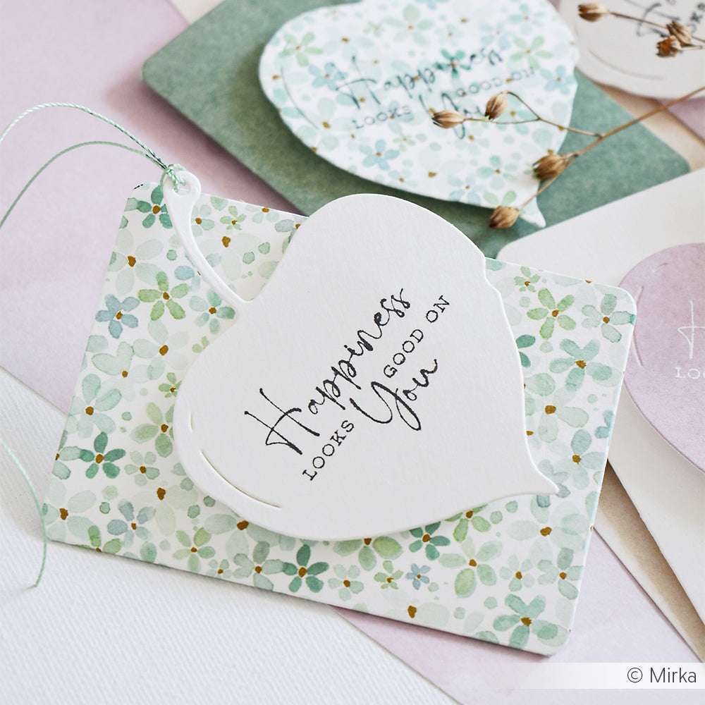 Herzförmiger Anhänger mit der Aufschrift "Das Glück steht dir gut" auf einer Karte mit Blumenmuster von Alexandra Renke und anderen Papieren - ideal für kreative Projekte mit Ihren Lieblingsholzstempeln und Stempelkissen.