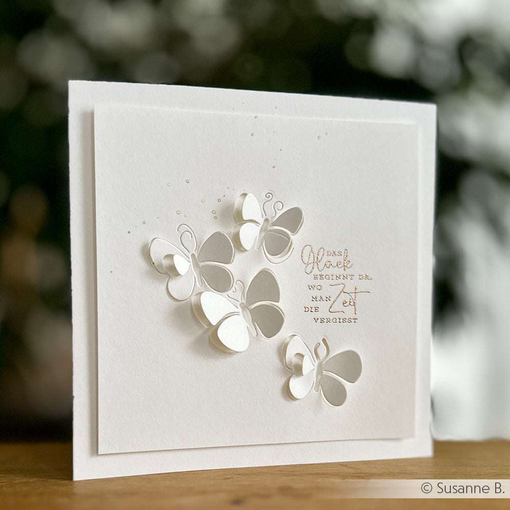 Weiße Grußkarte von Alexandra Renke mit erhabenen Schmetterlingen aus Papier, deutschem Text und zarten gestempelten Motiven auf einem weichzeichnenden Hintergrund.