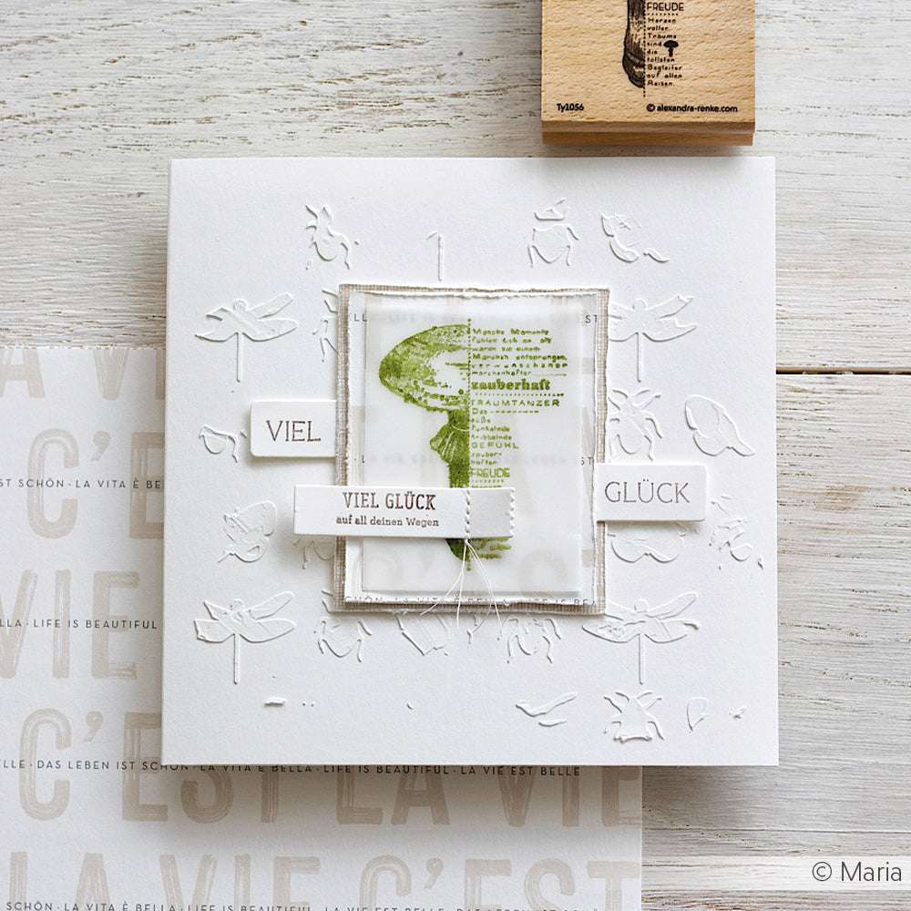 Handgefertigte Karte von Alexandra Renke mit geprägten Libellen, einem mit Stempelmotiv gestempelten grünen Baum und dem deutschen Text "Viel Glück" auf weißem Hintergrund.