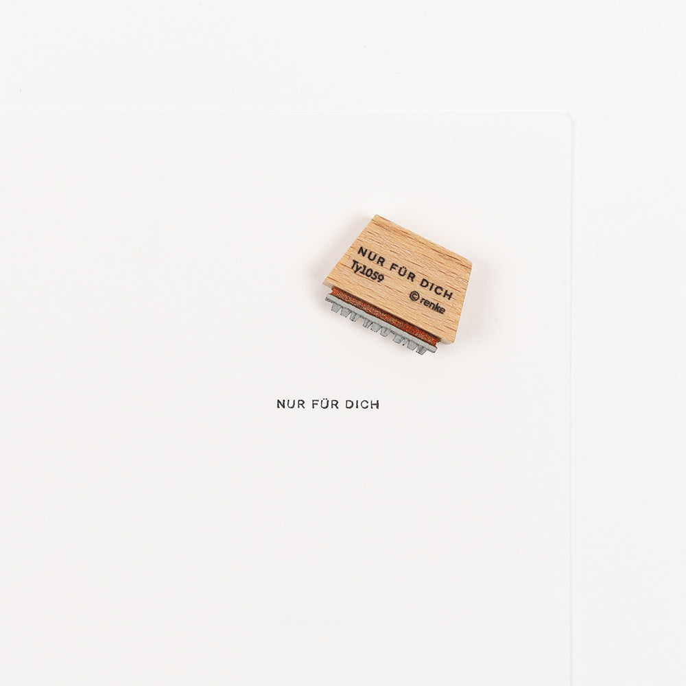 Ein Holzstempel und ein Blatt Papier, auf denen jeweils der Text „NUR FÜR DICH“ in der Schriftart „Mini Typo“ auf weißem Hintergrund zu sehen ist.