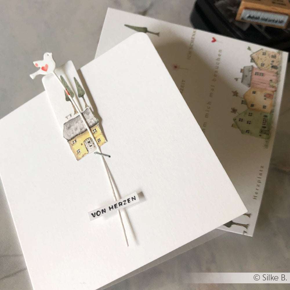 Weiße Grußkarte von Alexandra Renke mit einem kleinen Haus, Bäumen, einem Vogel und dem Schriftzug "VON HERZEN" - ideal für Papierprojekte oder zum Personalisieren mit Ihrem Lieblingsholzstempel.