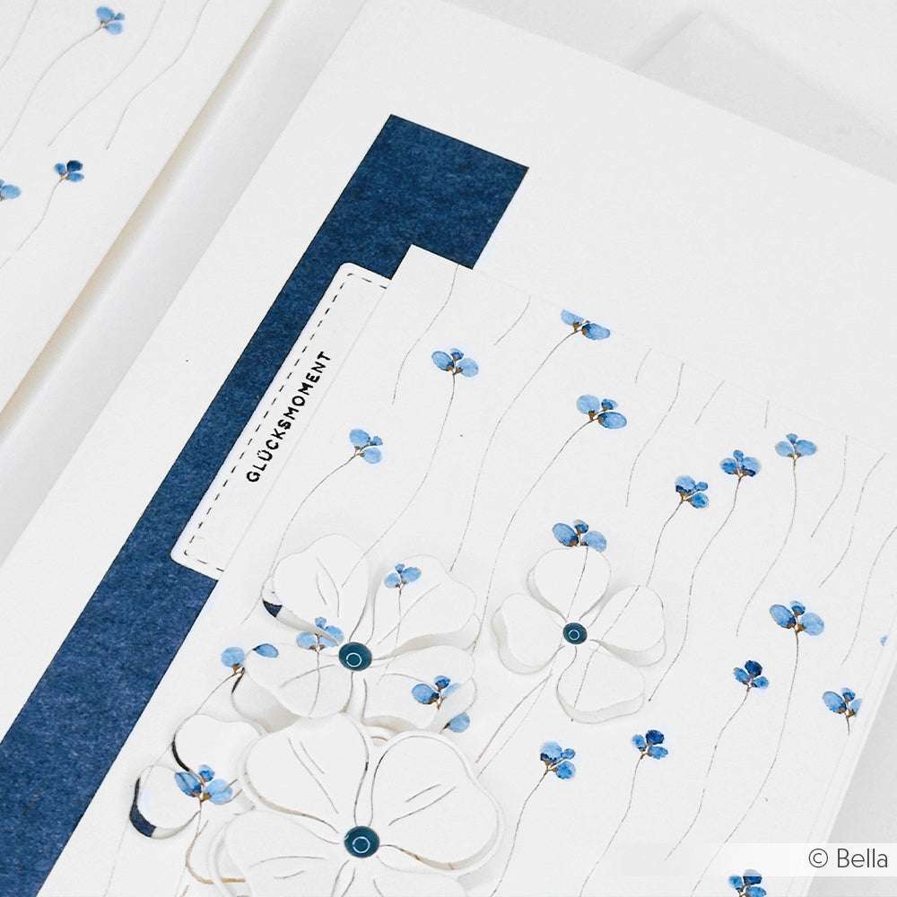 Eine handgefertigte Karte von Alexandra Renke mit weißen und blauen Blumen auf strukturiertem weißem Papier, überlagert auf blauem Hintergrund - ideal für Papierprojekte oder für Ihre bevorzugten Stempelkissen- und Holzstempeltechniken.