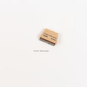 Ein Holzstempel mit Holzgriff, auf dem unten auf weißem Hintergrund „HAPPY BIRTHDAY“ aufgedruckt ist – ideal für die Verwendung mit Ihrem Lieblings-Stempelkissen.