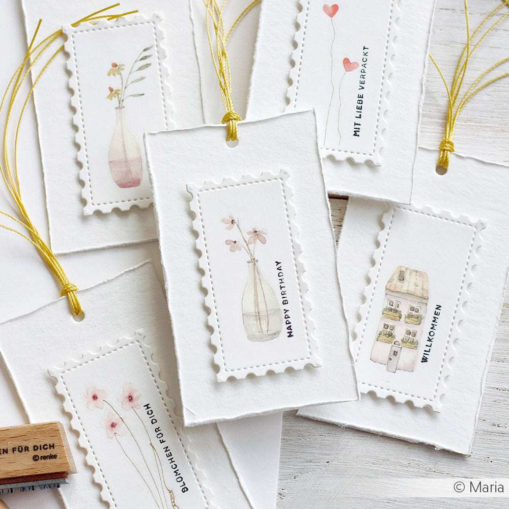 Die handgefertigten Karten von Alexandra Renke mit zarten Aquarellmotiven, gelber Schnur und deutschem Text sind auf einer weißen Oberfläche angeordnet und setzen elegante Akzente, die eine charmante Note verleihen.