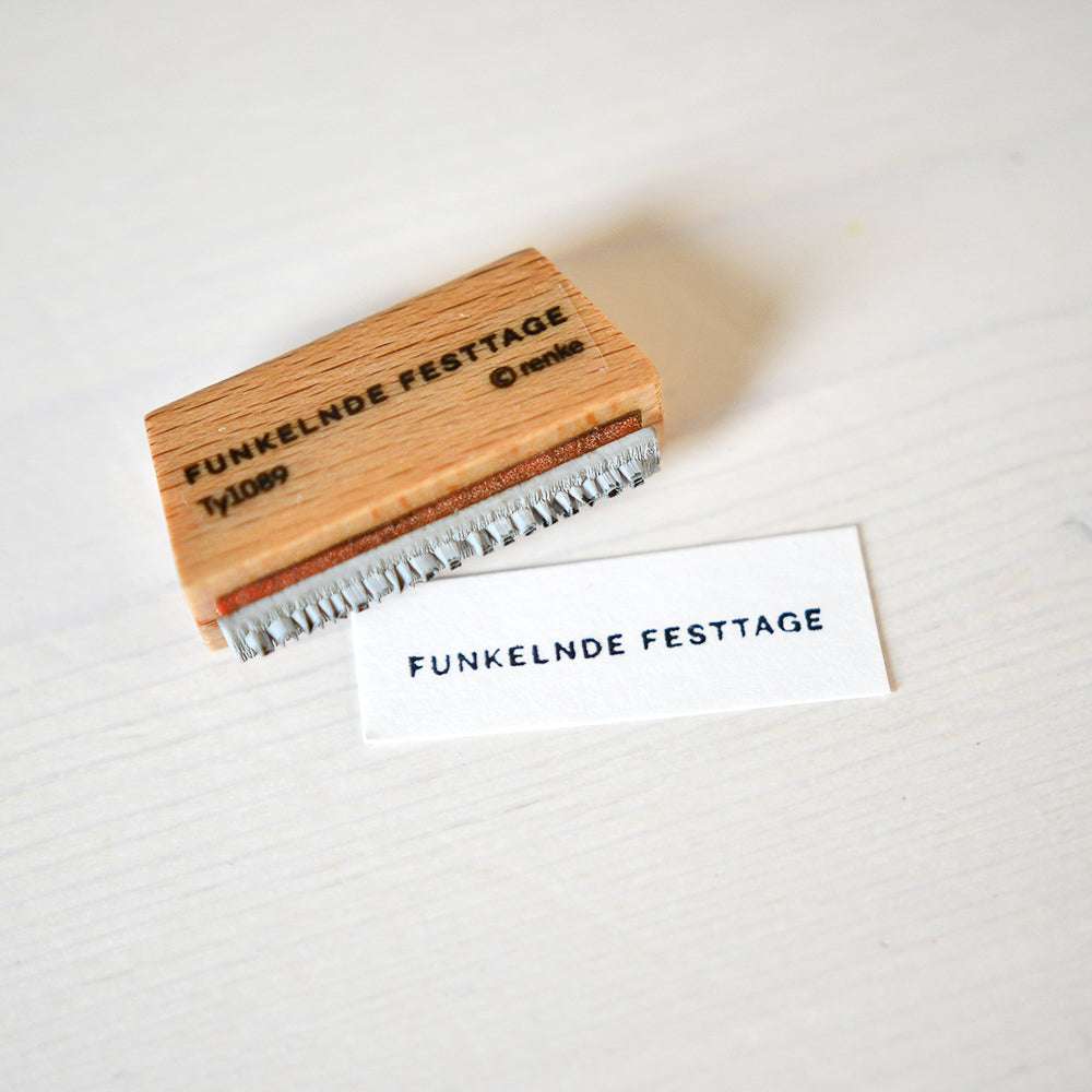 Ein Alexandra Renke Mini Typo Holzstempel und eine Karte zeigen beide den Text FUNKELNDE FESTTAGE auf einem hellen Hintergrund.