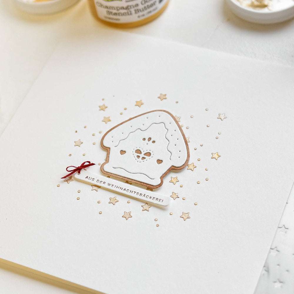 Eine handgefertigte Karte von Alexandra Renke mit einem Design aus vereisten Keksen, goldenen Sternen, dem Text "Aus der Weihnachtsbäckerei" und charmanten Details, die mit Stempelgummi erstellt wurden.