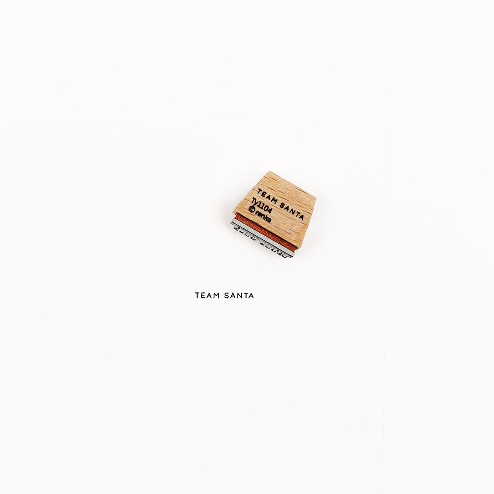Ein Holzstempel mit der Aufschrift TEAM SANTA und dem dazugehörigen Stempelabdruck.