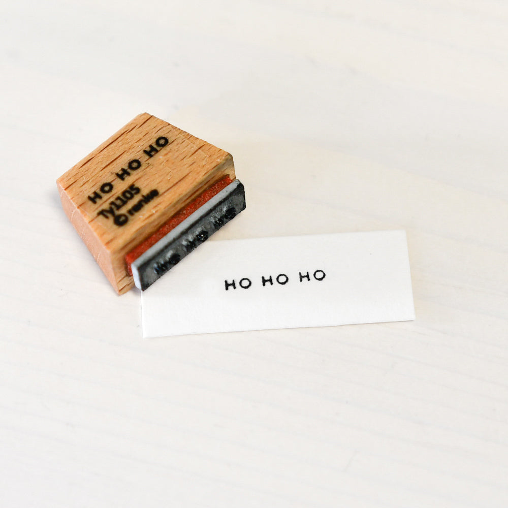 Ein Holzstempel und sein Tintenabdruck mit den Worten HO HO HO.
