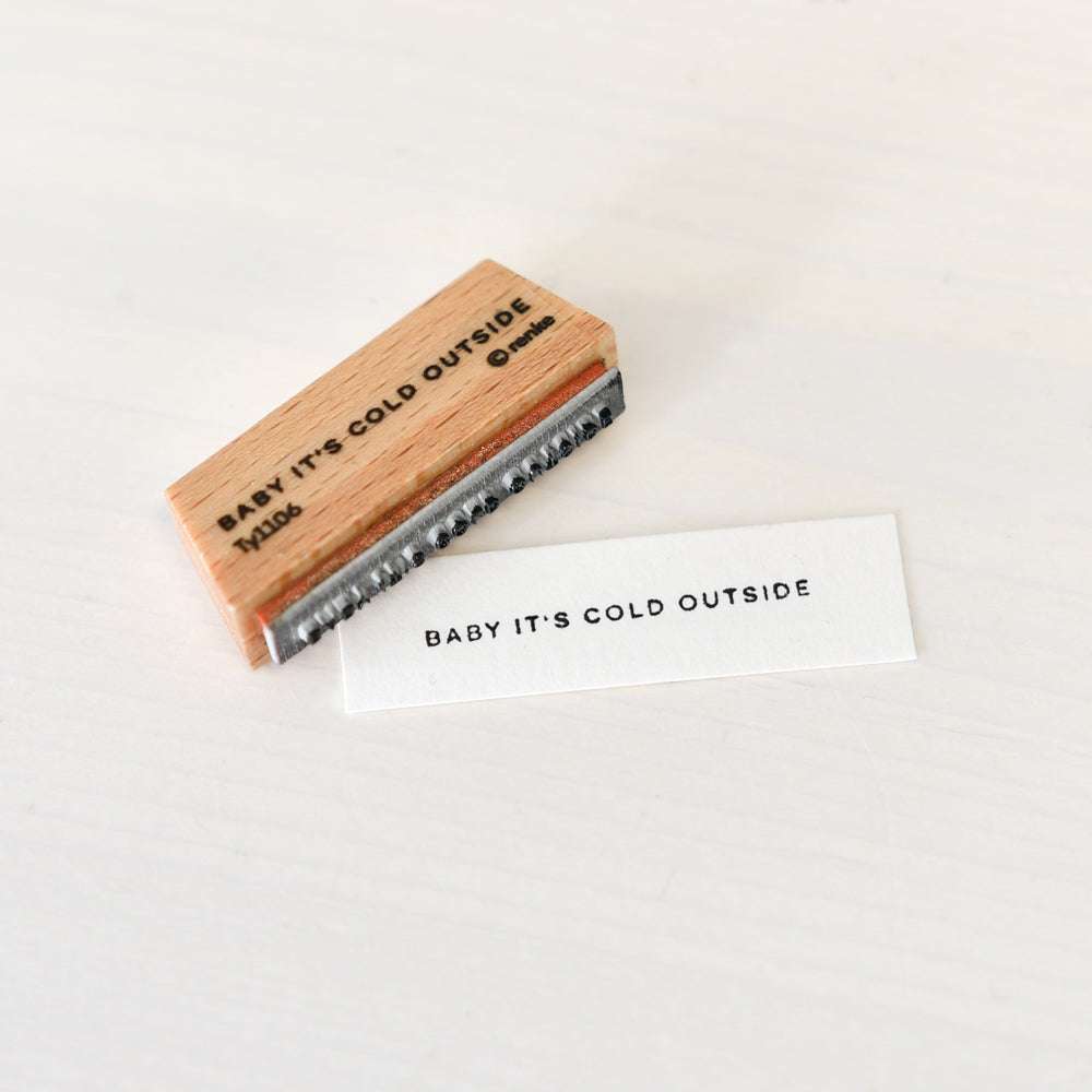 Ein Holzstempel von Alexandra Renke und eine gestempelte Karte mit der Aufschrift BABY ITS COLD OUTSIDE auf einer weißen Fläche - ideal für Ihre Papierprojekte oder kreative Ideen mit Stempelgummi.