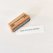 Ein Holzstempel von Alexandra Renke und eine gestempelte Karte mit der Aufschrift BABY ITS COLD OUTSIDE auf einer weißen Fläche - ideal für Ihre Papierprojekte oder kreative Ideen mit Stempelgummi.