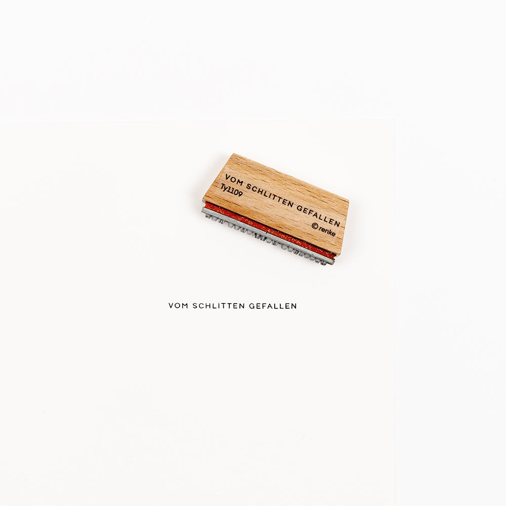 Ein Holzstempel mit der Aufschrift VOM SCHLITTEN GEFALLEN für Papierprojekte.