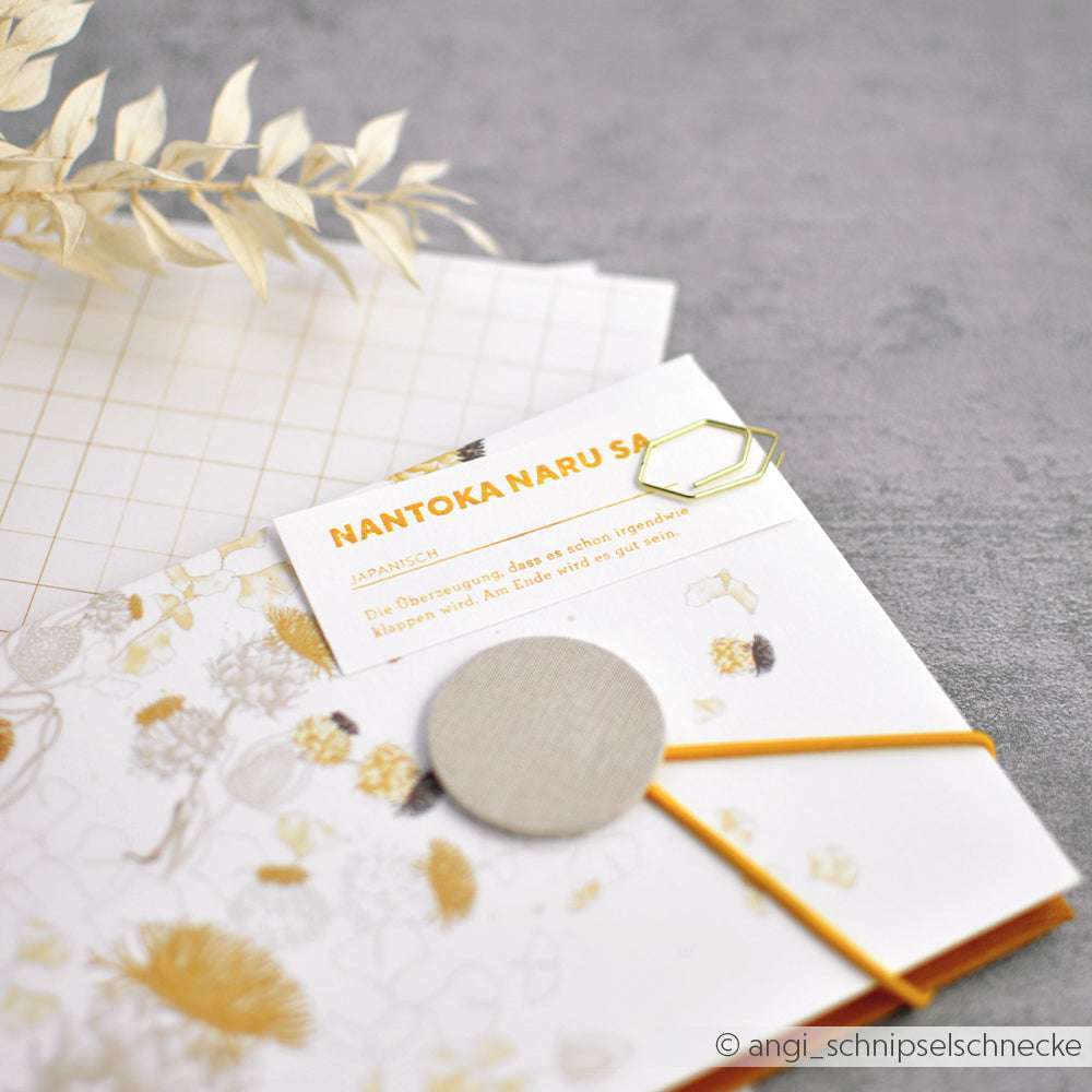 Briefpapier von Alexandra Renke mit Rasterpapier, getrockneten Blättern, einer NANTOKA NARU SA-Karte und Holzstempel - ideal für Papierprojekte oder zum Stempeln Ihrer Lieblingsmotive auf einer grauen Fläche.