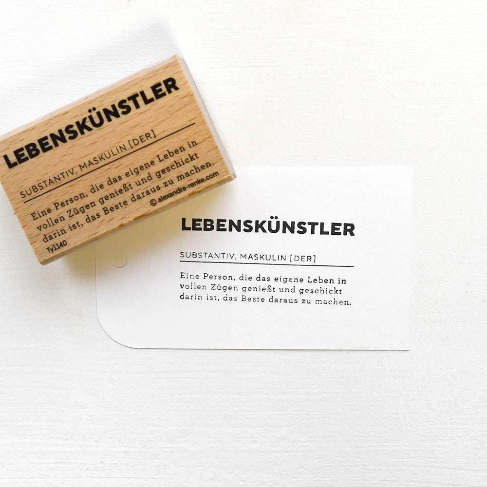 Ein Holzstempel von Alexandra Renke mit der Aufschrift "Lebenskünstler" und detailreichem Motiv - ideal für kreative Papierprojekte und individuelle Gestaltungen.