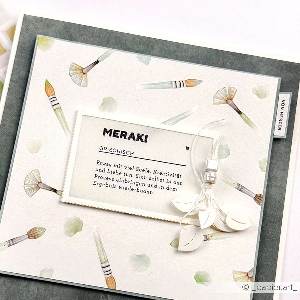 Eine Karte von Alexandra Renke mit Pinselillustrationen, "MERAKI" und einer deutschen Definition auf einem weißen Etikett - ideal für Holzstempel-Fans und Papierprojekte.