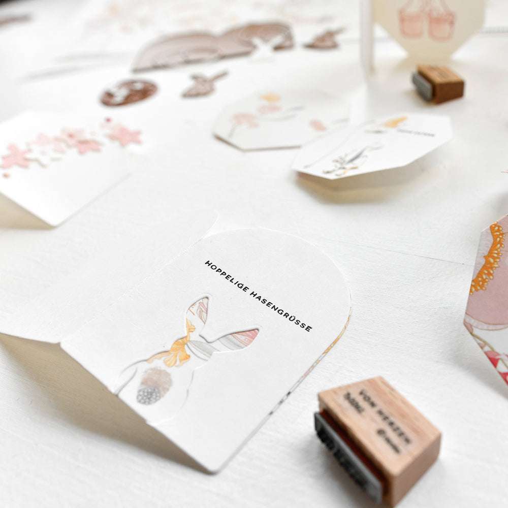 Nahaufnahme von illustrierten Papierbasteleien, Alexandra Renke Mini Typo Stempeln und Hoppelige Hasengrüße Ausschnitten auf einer weißen Fläche.