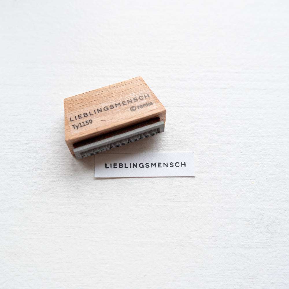 Alexandra Renke Holzstempel mit dem Schriftzug "LIEBLINGSMENSCH" liegt neben passendem Abdruck auf weißem Papier - ideal für kreative Papierprojekte.