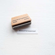 Der Alexandra Renke Holzstempel mit der Aufschrift Geburtstagspost ist neben gestanztem Text auf weißem Papier abgebildet, ideal für kreative Papierprojekte auf hellem Untergrund.