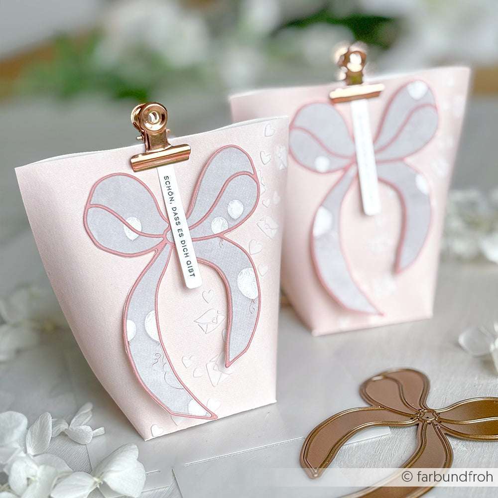 Zwei rosafarbene Geschenktüten mit weißen Bändern, die mit goldenen Klammern verschlossen sind, werden auf einer weißen Fläche präsentiert - eine charmante Idee von Alexandra Renke, um Stempel wie Stempelgummi oder Holzstempel in Szene zu setzen.