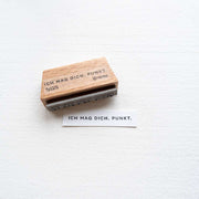 Ein Holzstempel von Alexandra Renke mit dem Motiv "ICH MAG DICH. PUNKT." und gestempeltes Papier liegen auf weißem Untergrund - ein passendes Stempelkissen sorgt für klare Ergebnisse.